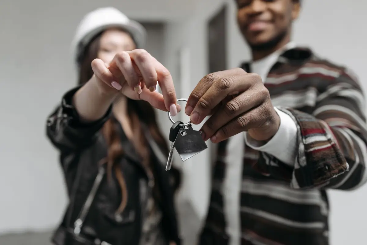 Two people holding up a single house key on a ring with a small metal house-shaped tag